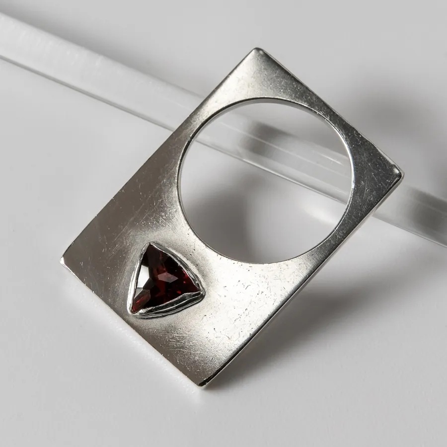 Original photo: a flat silver ring with a triangular garnet, lying on a greyish light surface