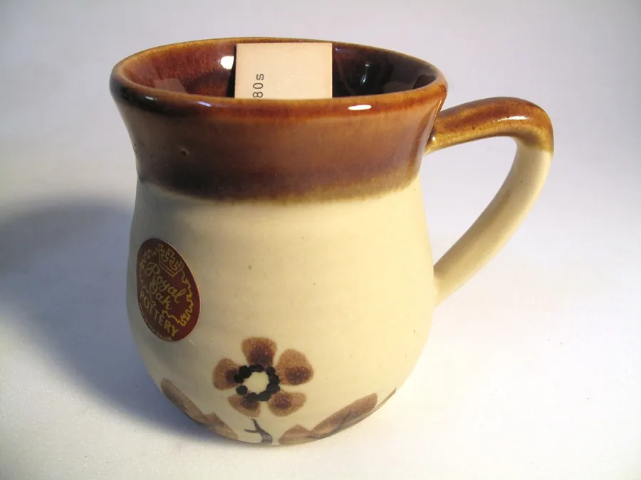 Original photo: a brown and cream stoneware mug with a painted flower, on a poorly lit greyish white background