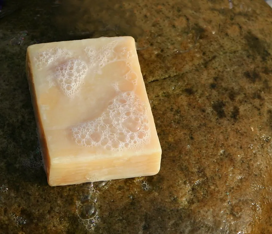 Original photo: a cream handmade soap bar covered in foam, lying on a wet stone